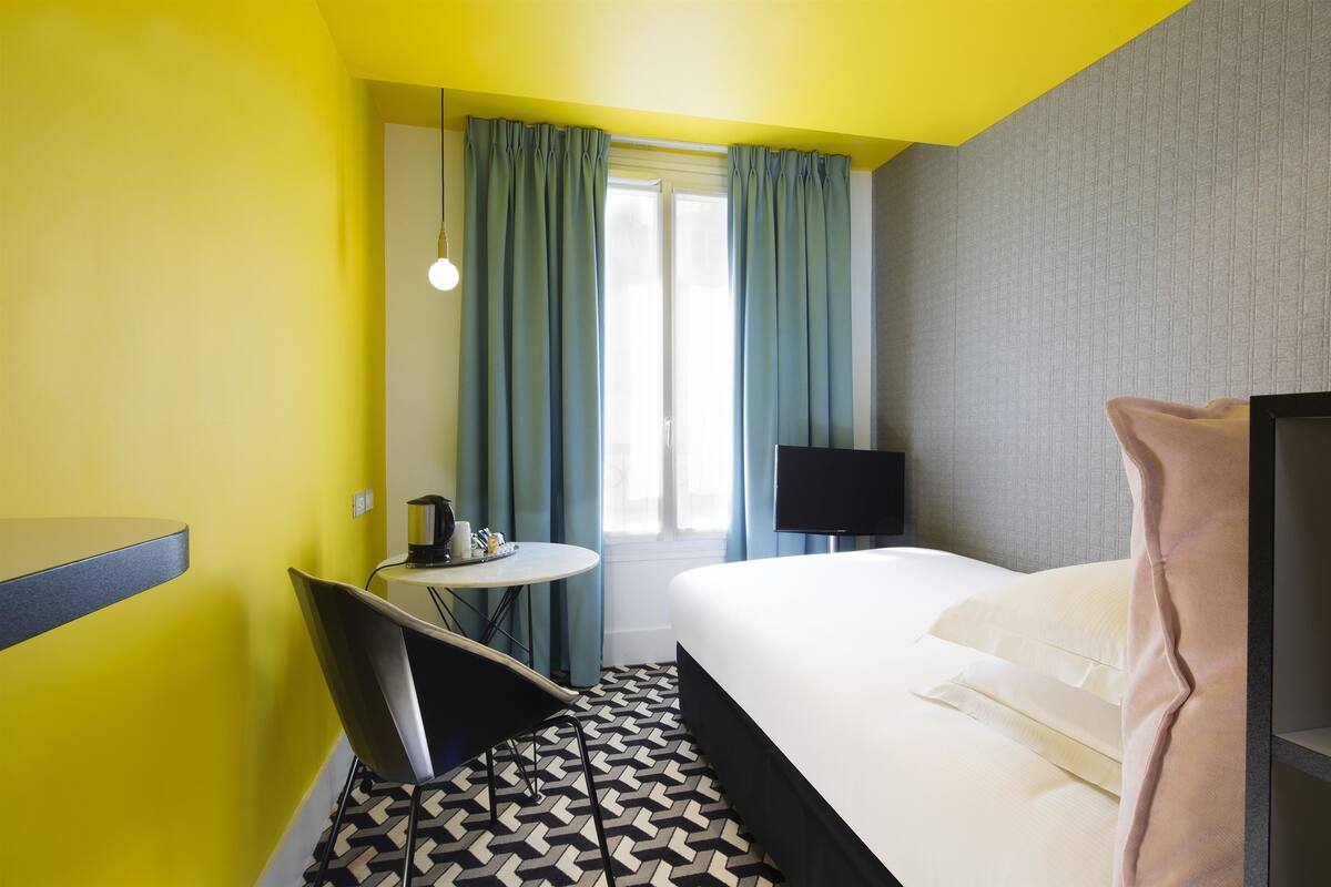 A hotel room with a bed, a desk, a chair, a TV, and a window with curtains.