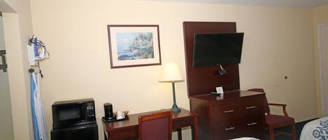 Habitación de hotel con cama, escritorio con computadora, microondas, televisor, silla y cómoda.