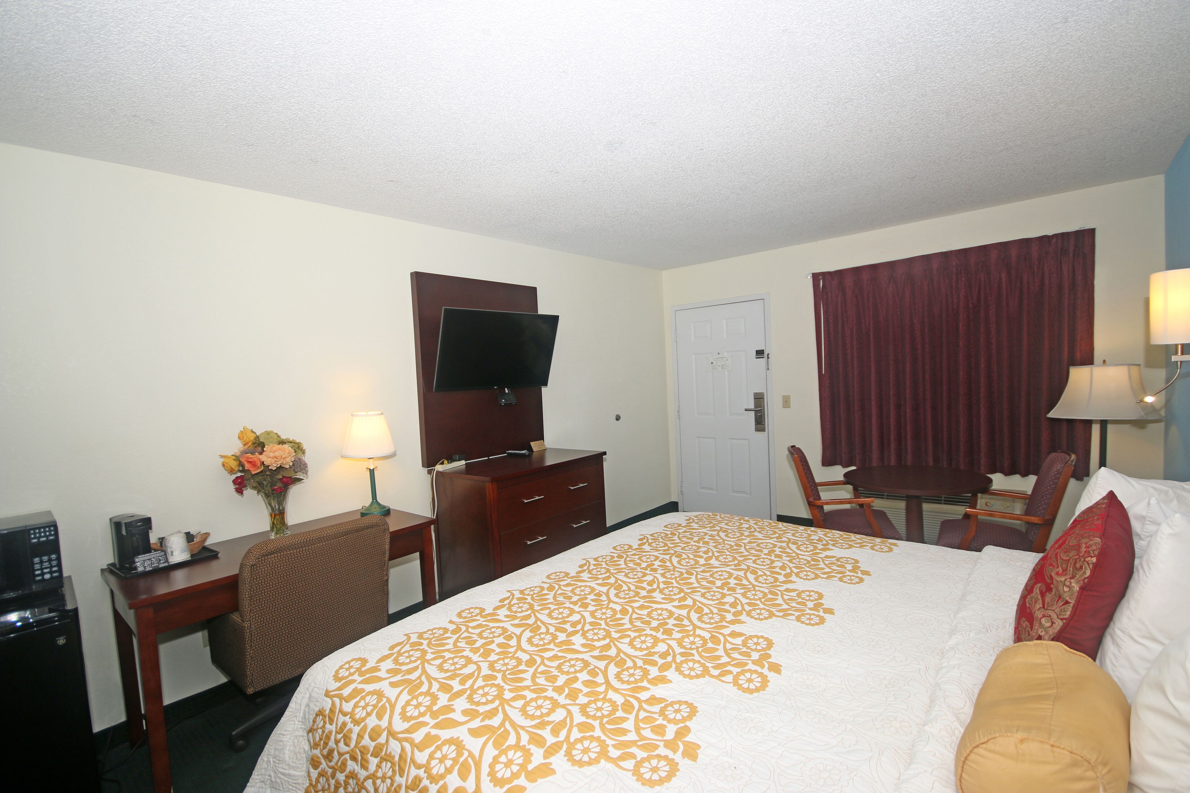 Habitación de hotel con cama, escritorio con computadora, televisor, silla, mesa y lámpara.