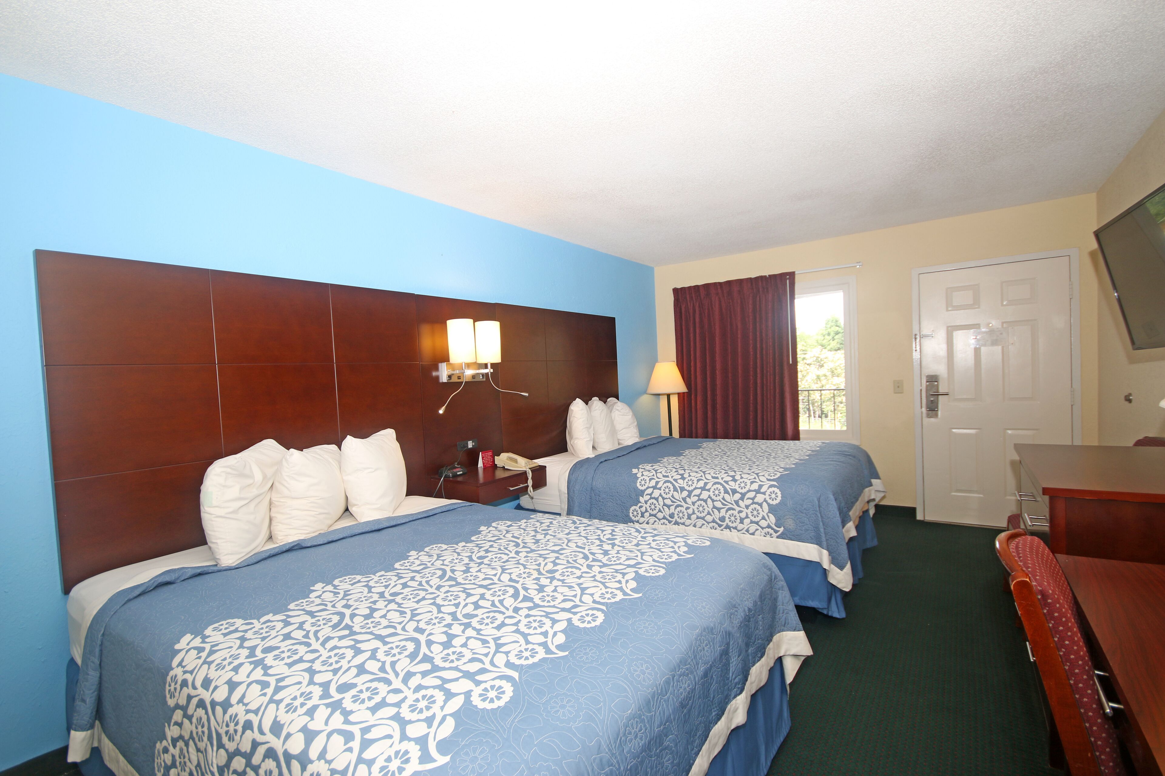 A hotel room with two beds, a wooden headboard, a desk, and a television.