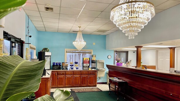 A hotel reception area with a wooden counter, a coffee machine, and a chandelier. - Hamilton Inn Jonesville NC (Jonesville)
