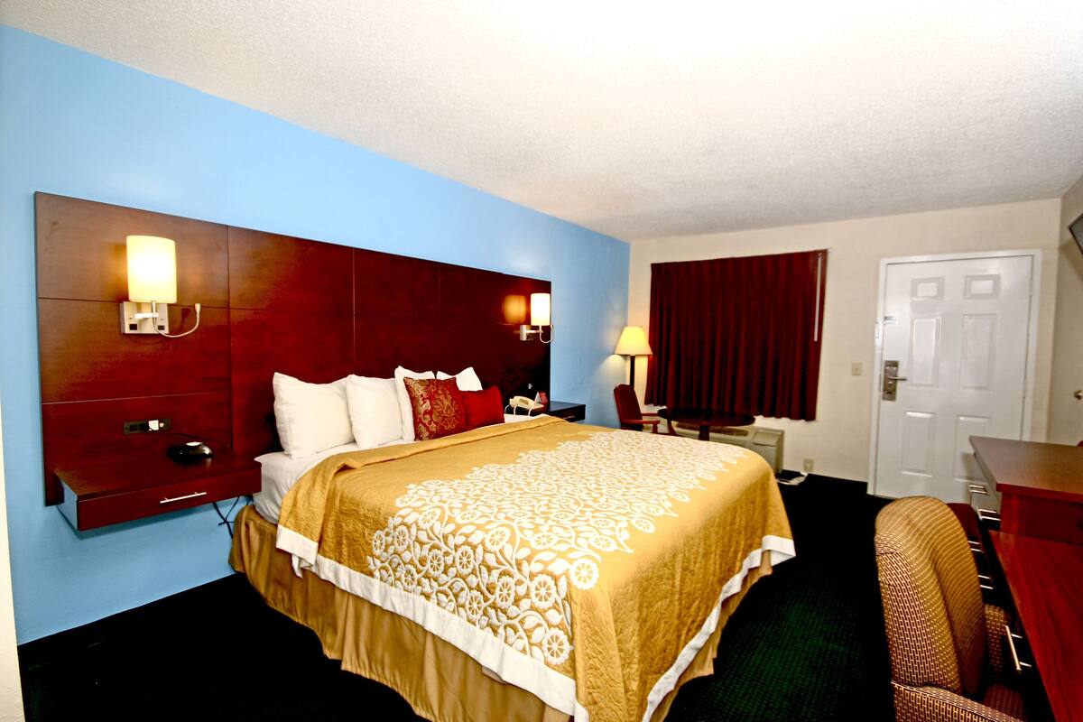 A hotel room with a large bed, a desk, a chair, and a wardrobe.