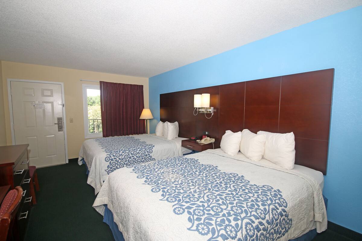 A hotel room with two beds, a desk, and a nightstand with a lamp.
