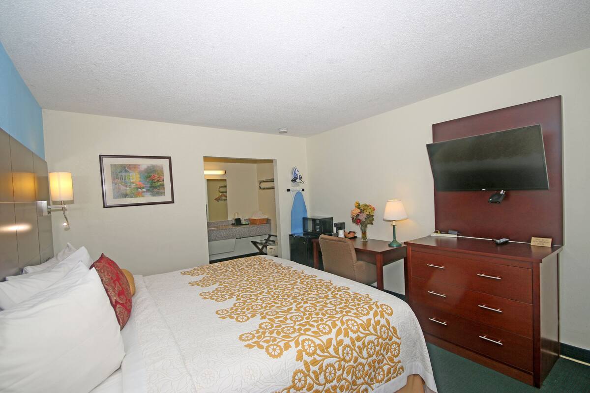A hotel room with a bed, a desk, a dresser, a TV, and a painting on the wall.
