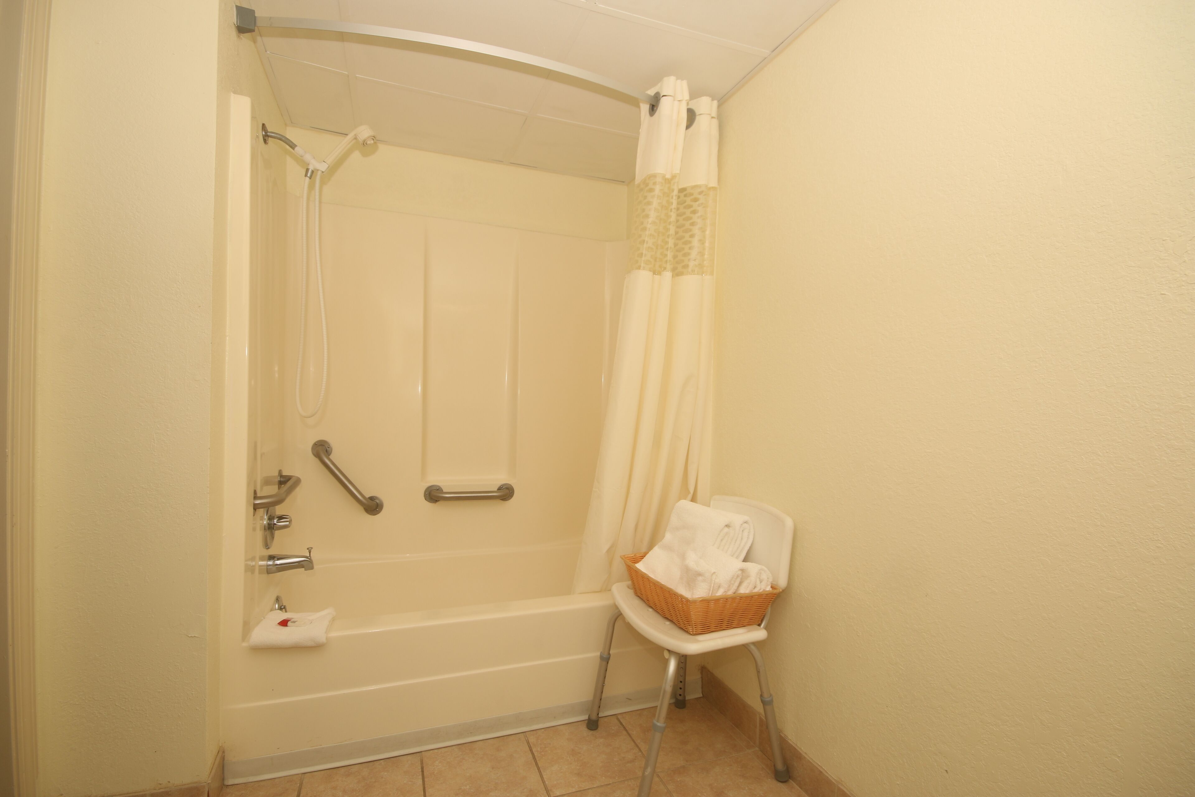 A bathroom with a bathtub, shower, and a wheelchair-accessible chair.