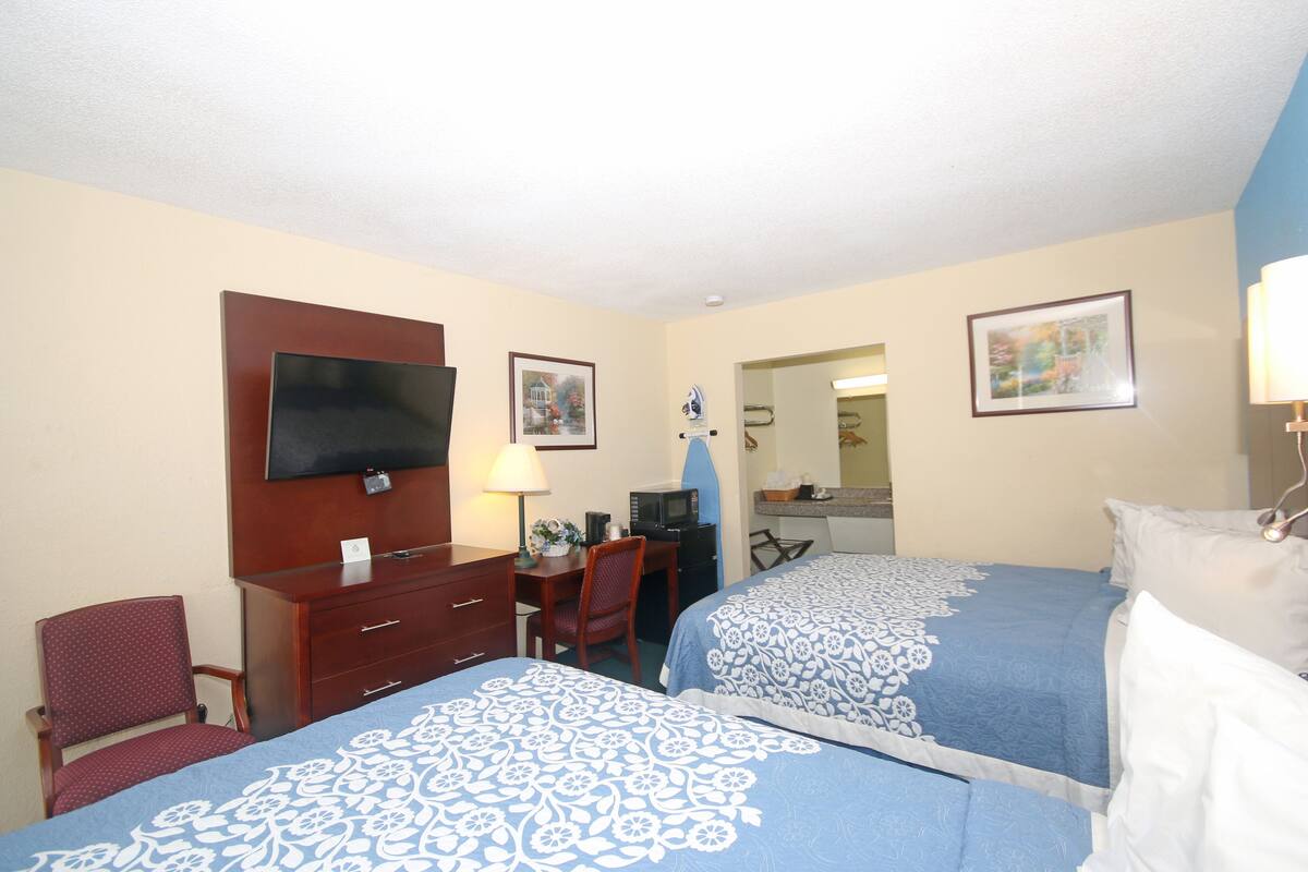A hotel room with two beds, a desk, a chair, a TV, and a microwave.
