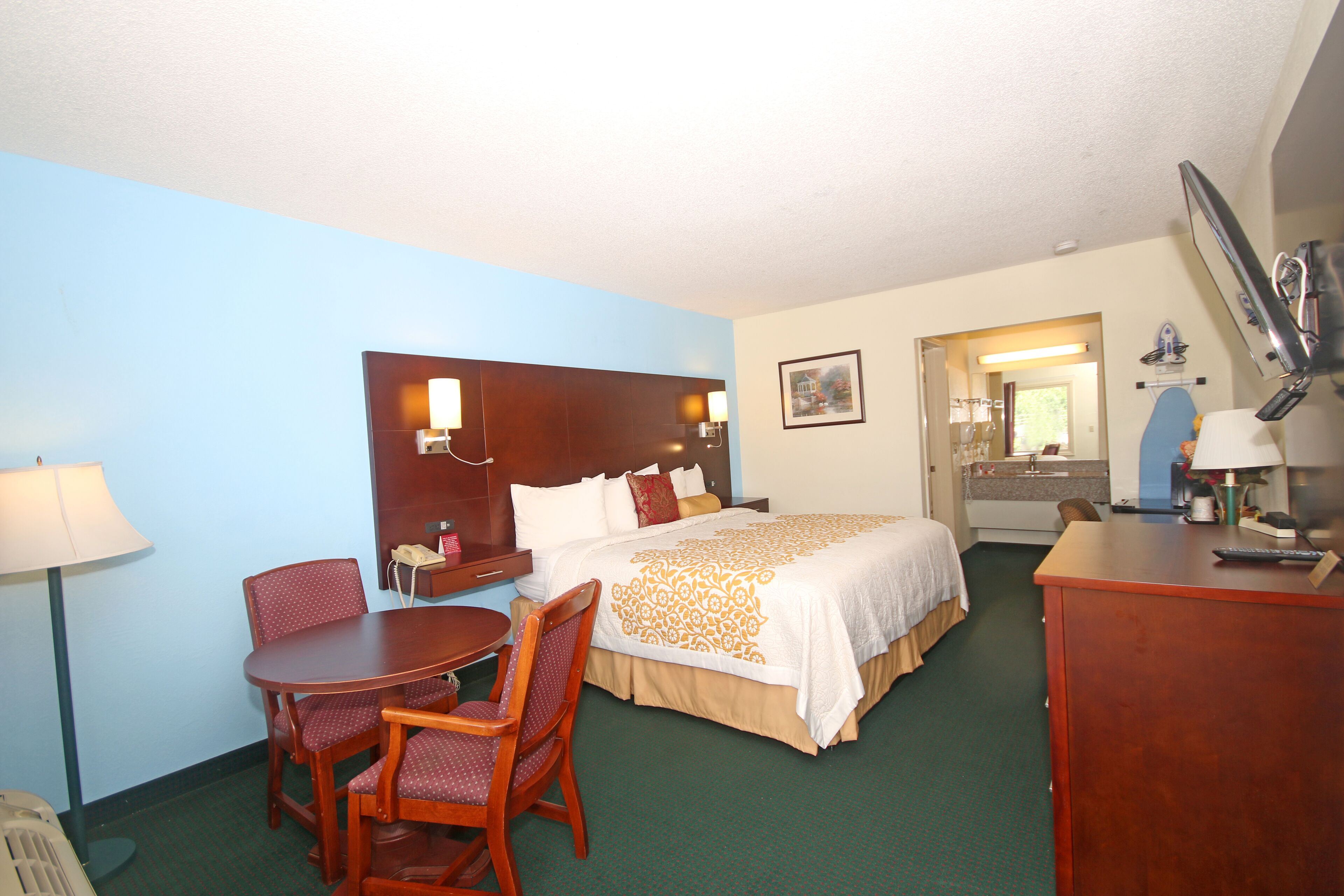 A hotel room with a bed, a desk, a chair, a lamp, and a mirror.