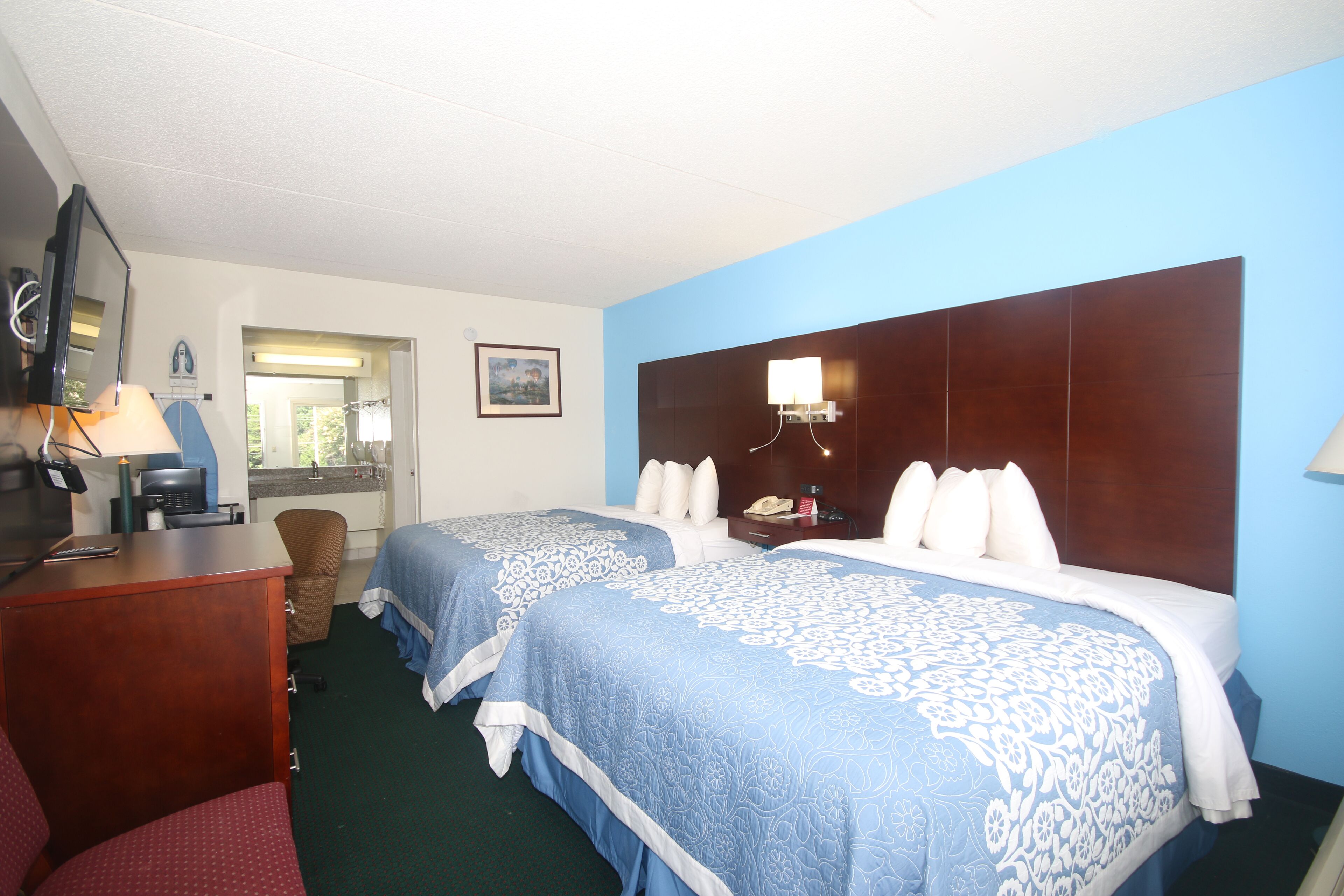 A hotel room with two beds, a desk with a lamp, a chair, a television, and a window with a view of the outdoors.