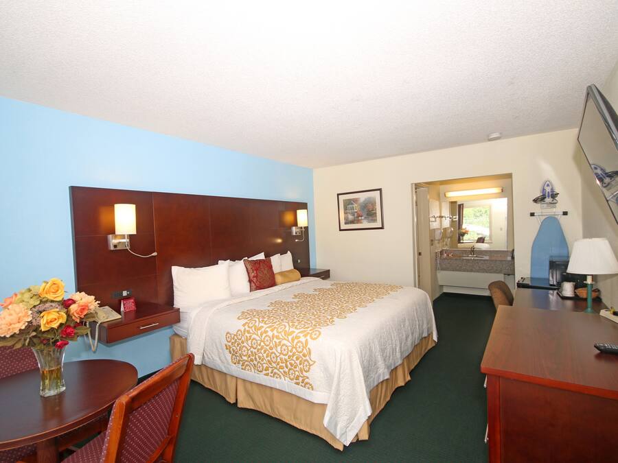 Een hotelkamer met een groot bed, een bureau, een stoel, een kleine tafel met een bloevas, en een badkamer die door een open deur zichtbaar is.