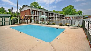 A rectangular pool with a surrounding deck, lounge chairs, and a building with multiple windows and a staircase. - Hamilton Inn Jonesville NC (Jonesville)