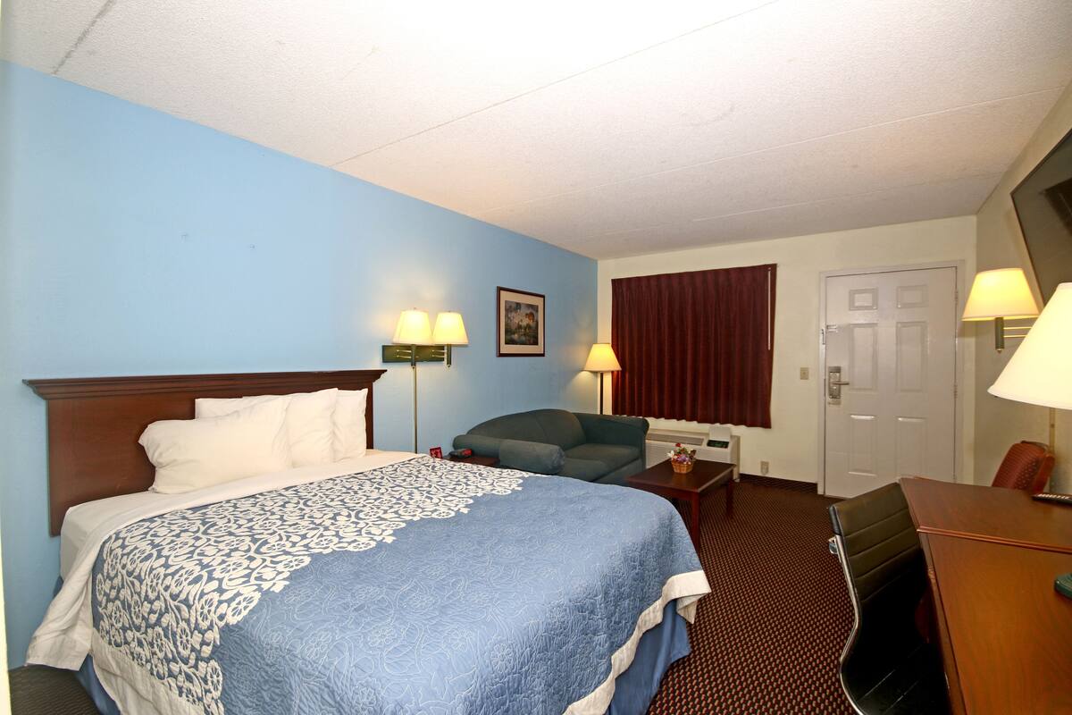A hotel room with a bed, a desk, a chair, and two lamps.
