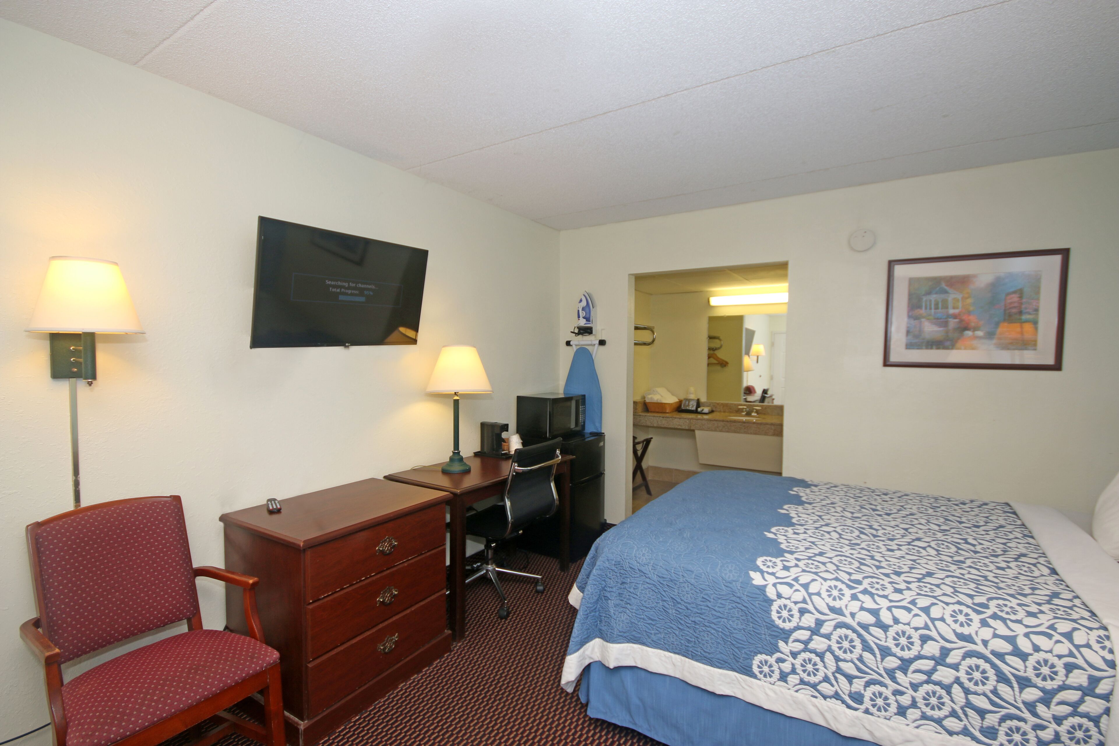 Une chambre d’hôtel comprenant un lit, un bureau, une chaise, une commode, une lampe de bureau et un tableau au mur.