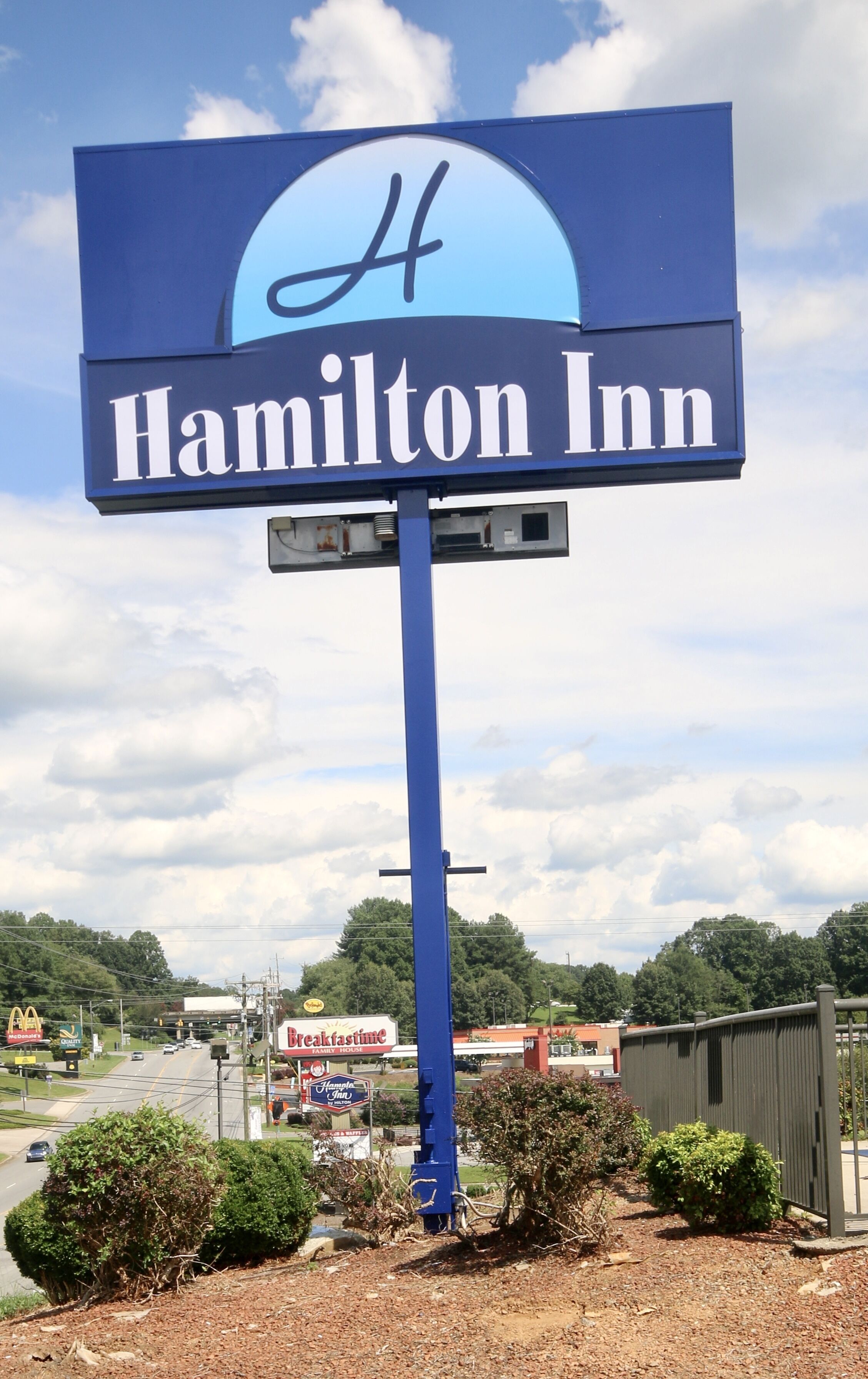Señal de Hamilton Inn con vista clara de los alrededores, incluyendo un McDonald's y un Breakfast House.