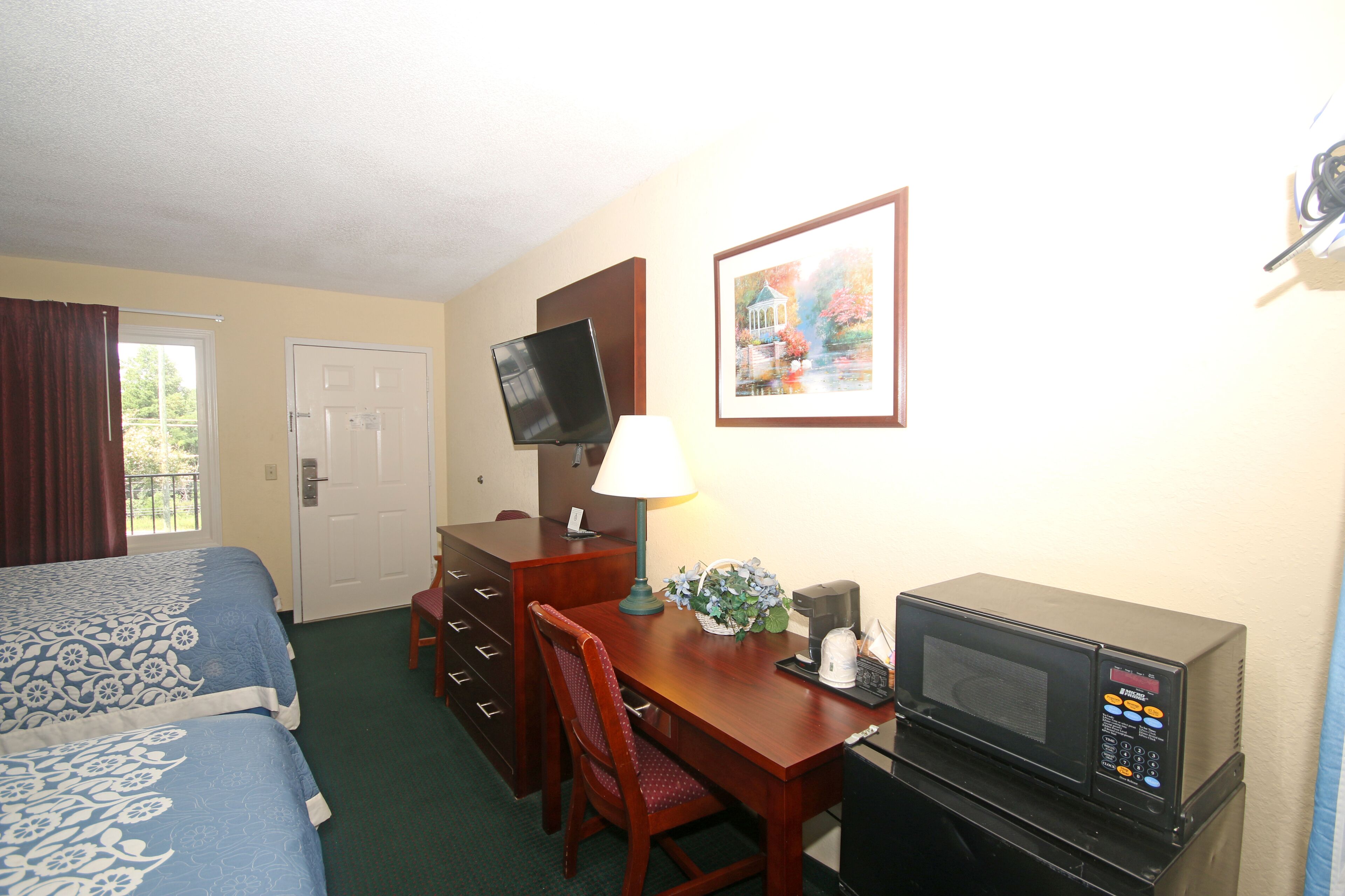 A hotel room with a bed, a desk with a computer, a microwave, and a television.