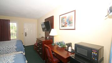A hotel room with a bed, a desk with a computer, a microwave, and a television.