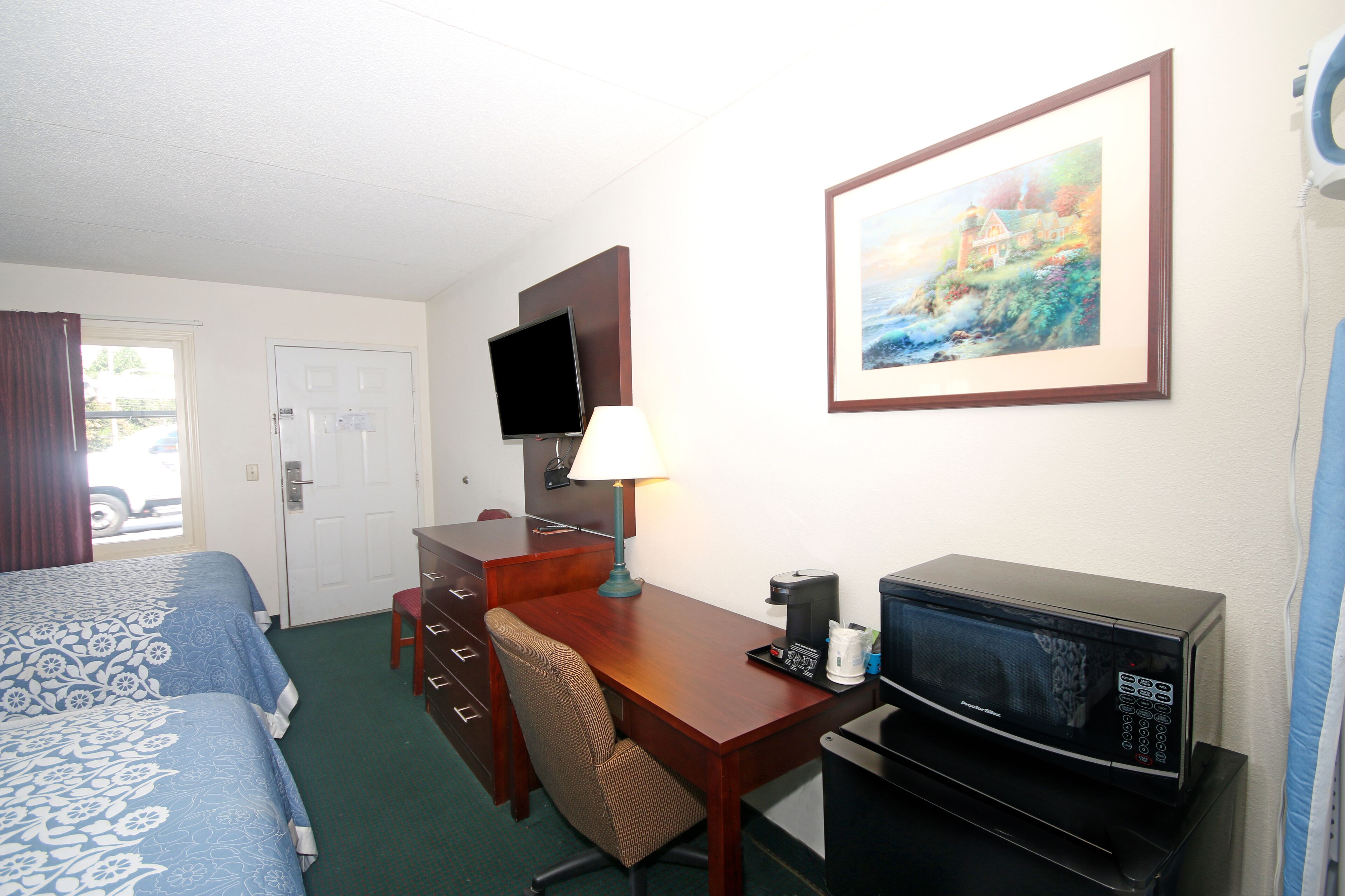 A hotel room with a bed, desk, chair, television, and microwave.