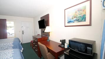A hotel room with a bed, desk, chair, television, and microwave.