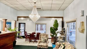 A reception area with a wooden reception desk, a chandelier, a dining area with chairs and a table, and a large potted plant. - Hamilton Inn Jonesville NC (Jonesville)