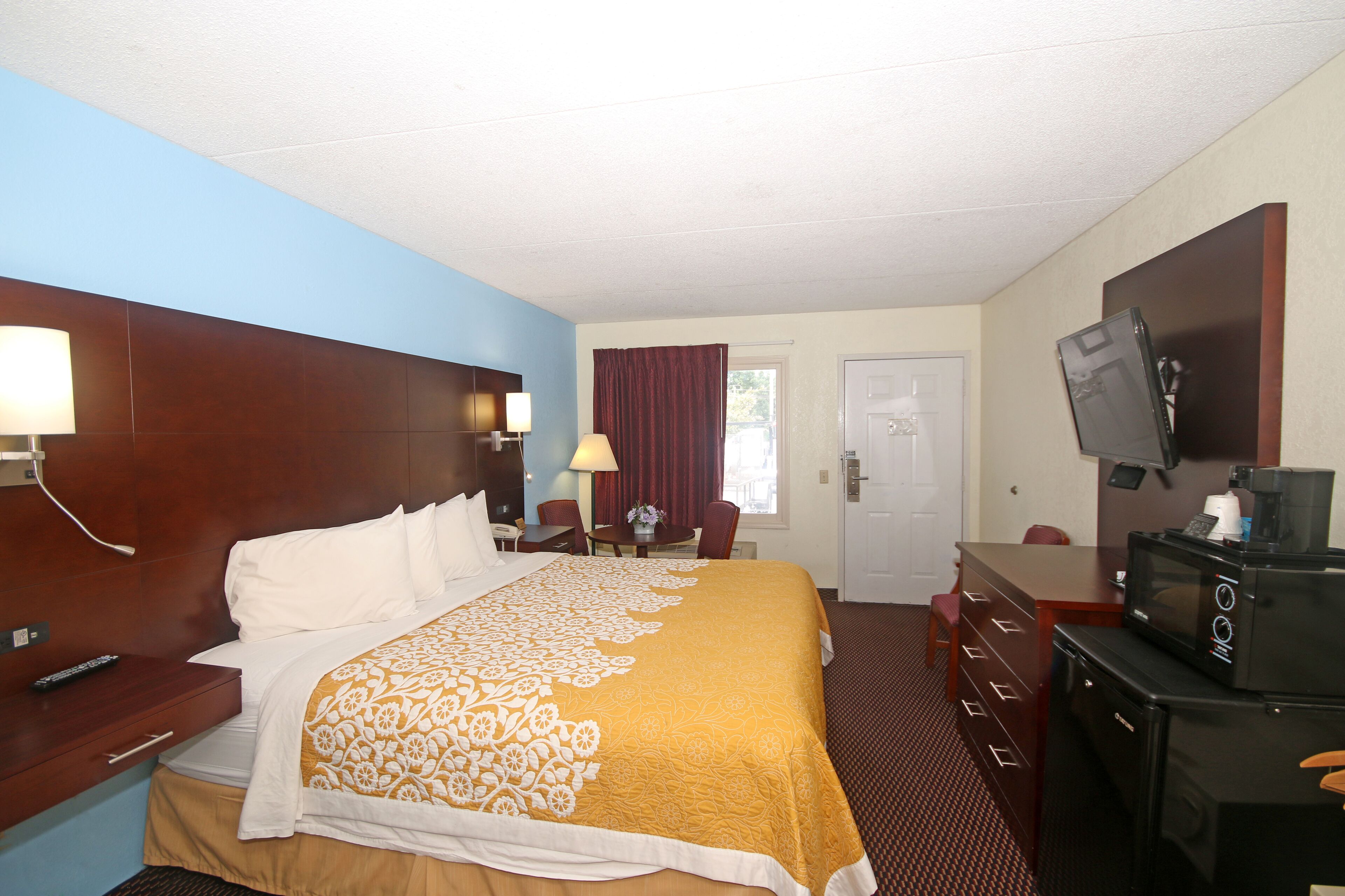 Habitación de hotel con una cama grande, un escritorio con silla, un televisor y un microondas.