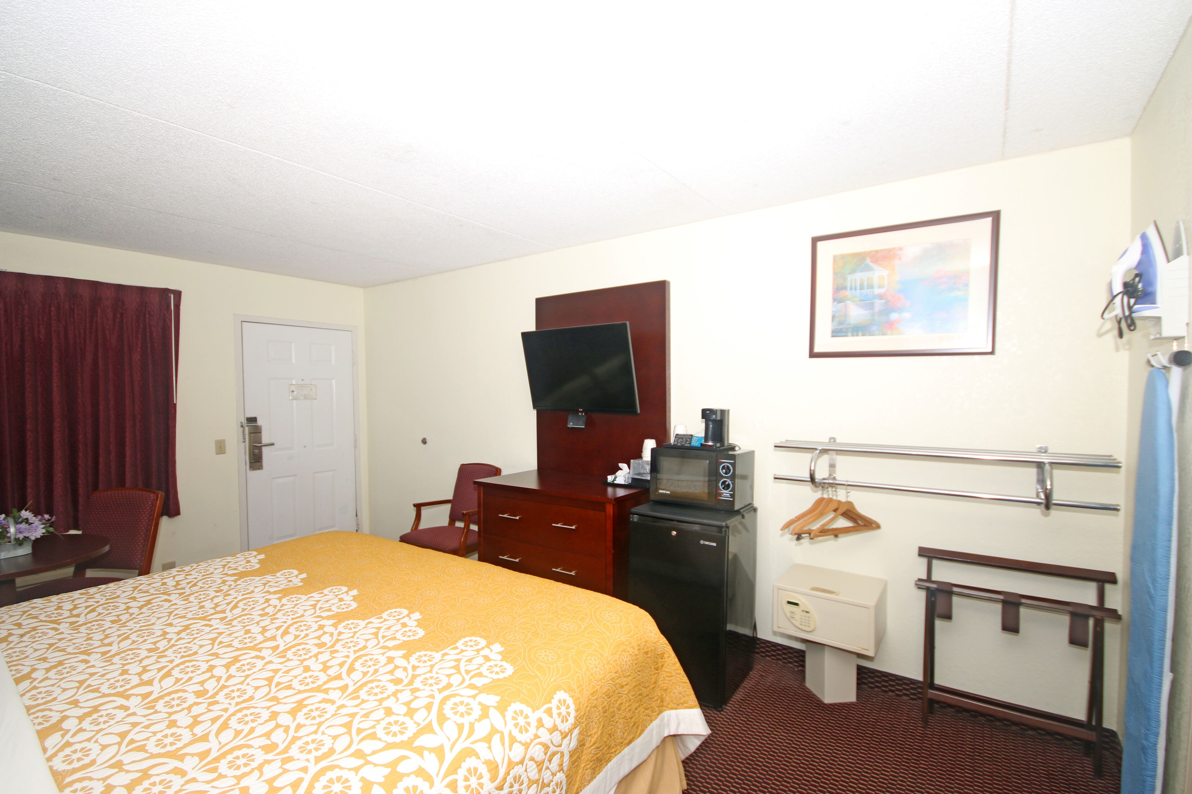 A hotel room with a bed, a desk, a television, a microwave, a coat rack, and a door.