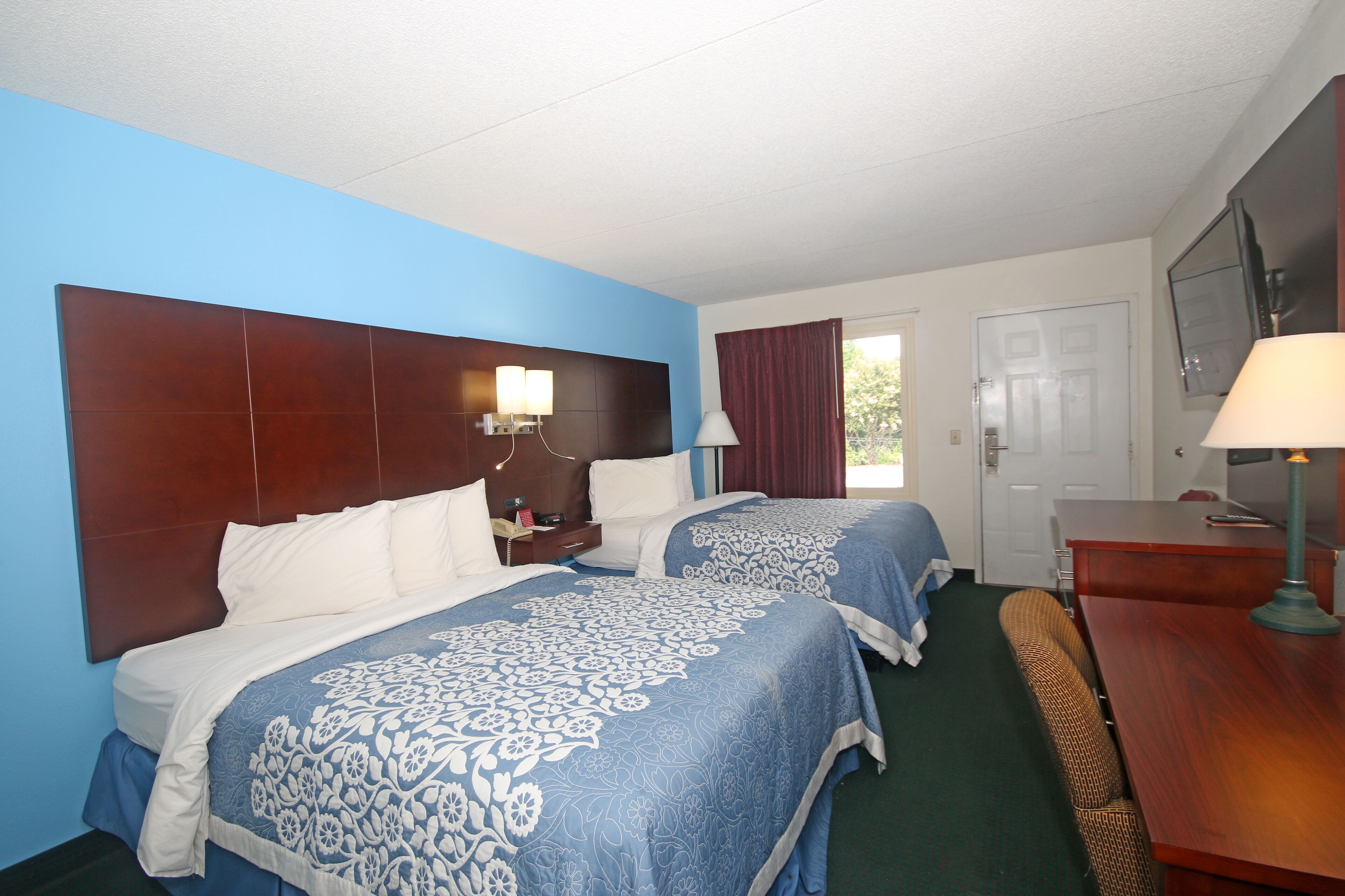 A hotel room with two beds, a desk, a chair, and a TV.