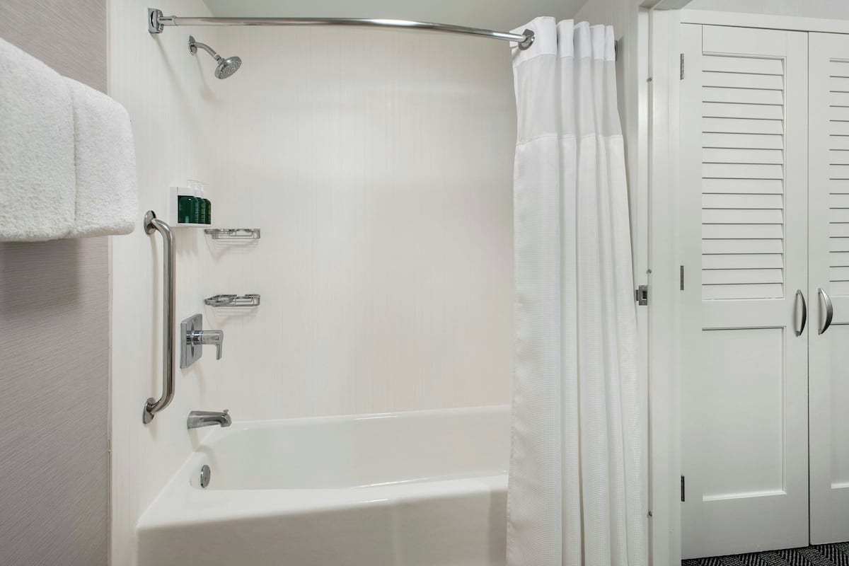 A bathroom with a white bathtub, a shower with a handheld showerhead, a grab bar, and a towel rack.