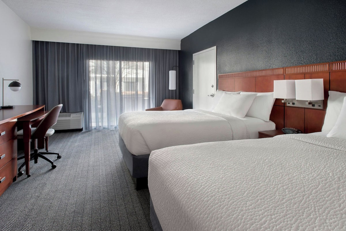 A hotel room with two beds, a desk, and a chair.