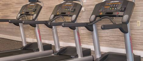 Three treadmills with digital displays, FlexDeck shock absorption system, and a wooden wall in the background.