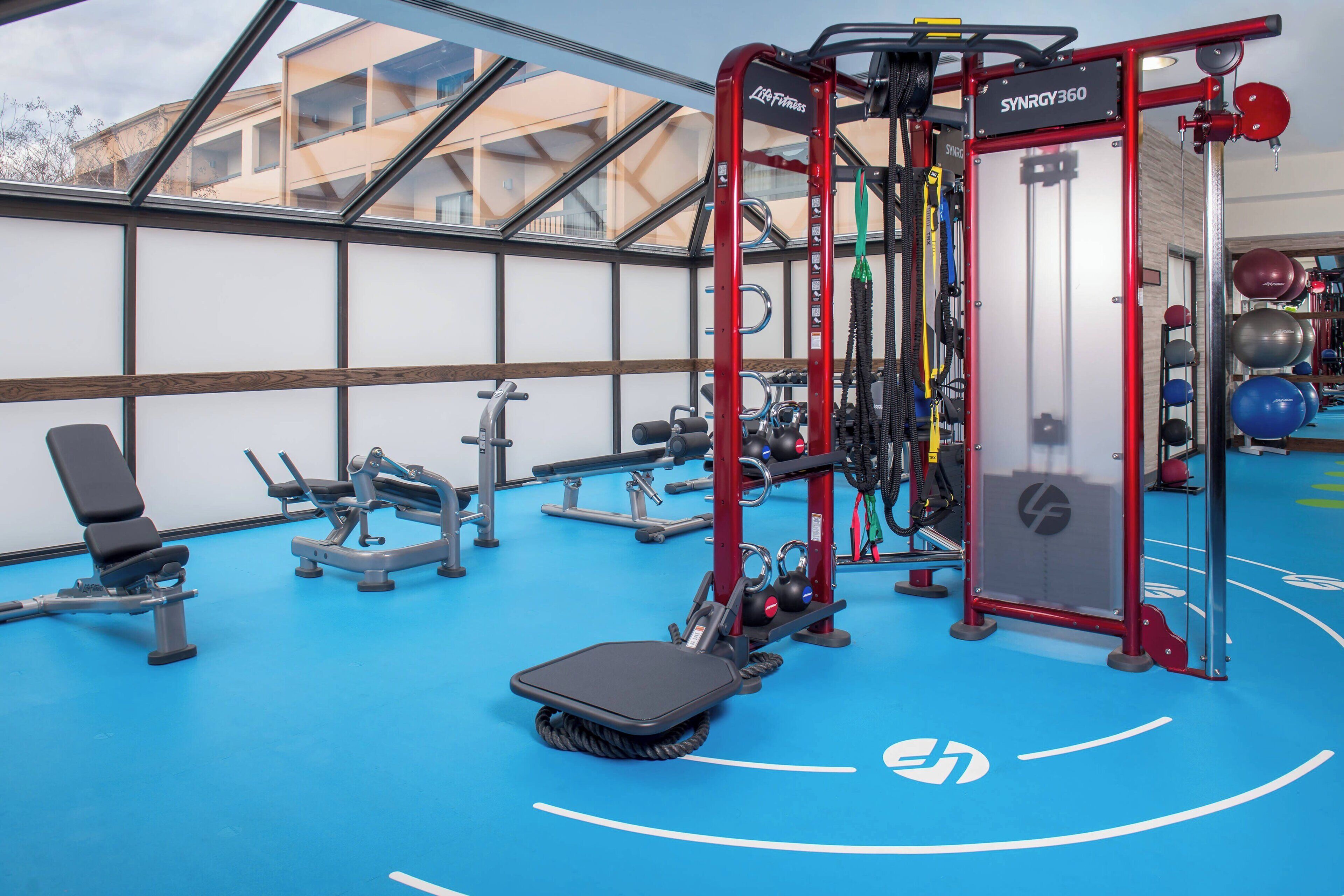 A gym with exercise equipment, a bench, and a blue floor with white lines.