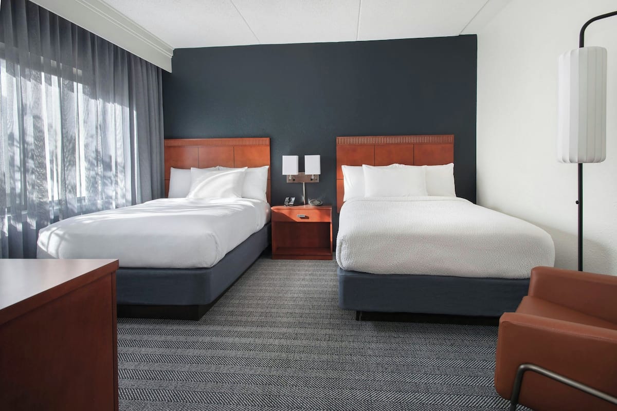 A hotel room with two beds, a nightstand, a desk, and a chair.