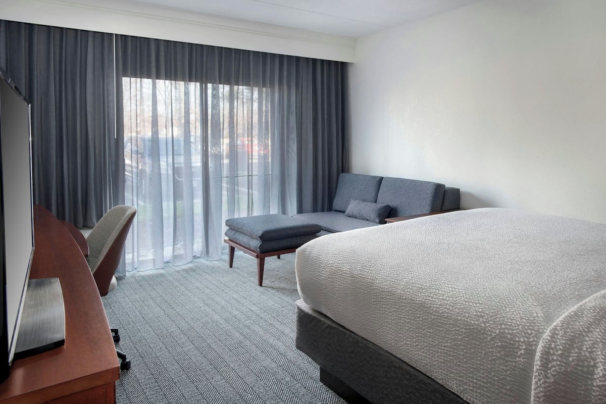 A hotel room with a large bed, a desk, a chair, and a sofa.