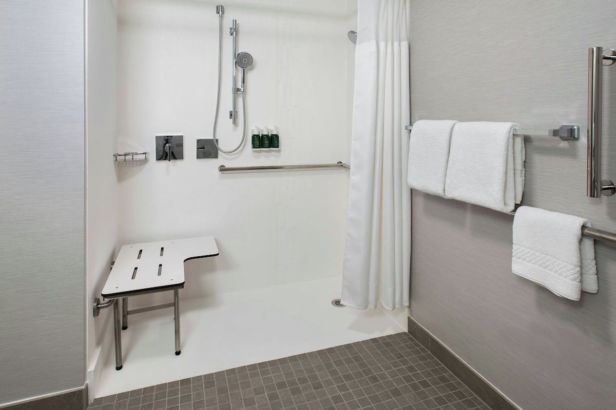 A modern bathroom with a shower, a small table, and two towels on a rack.