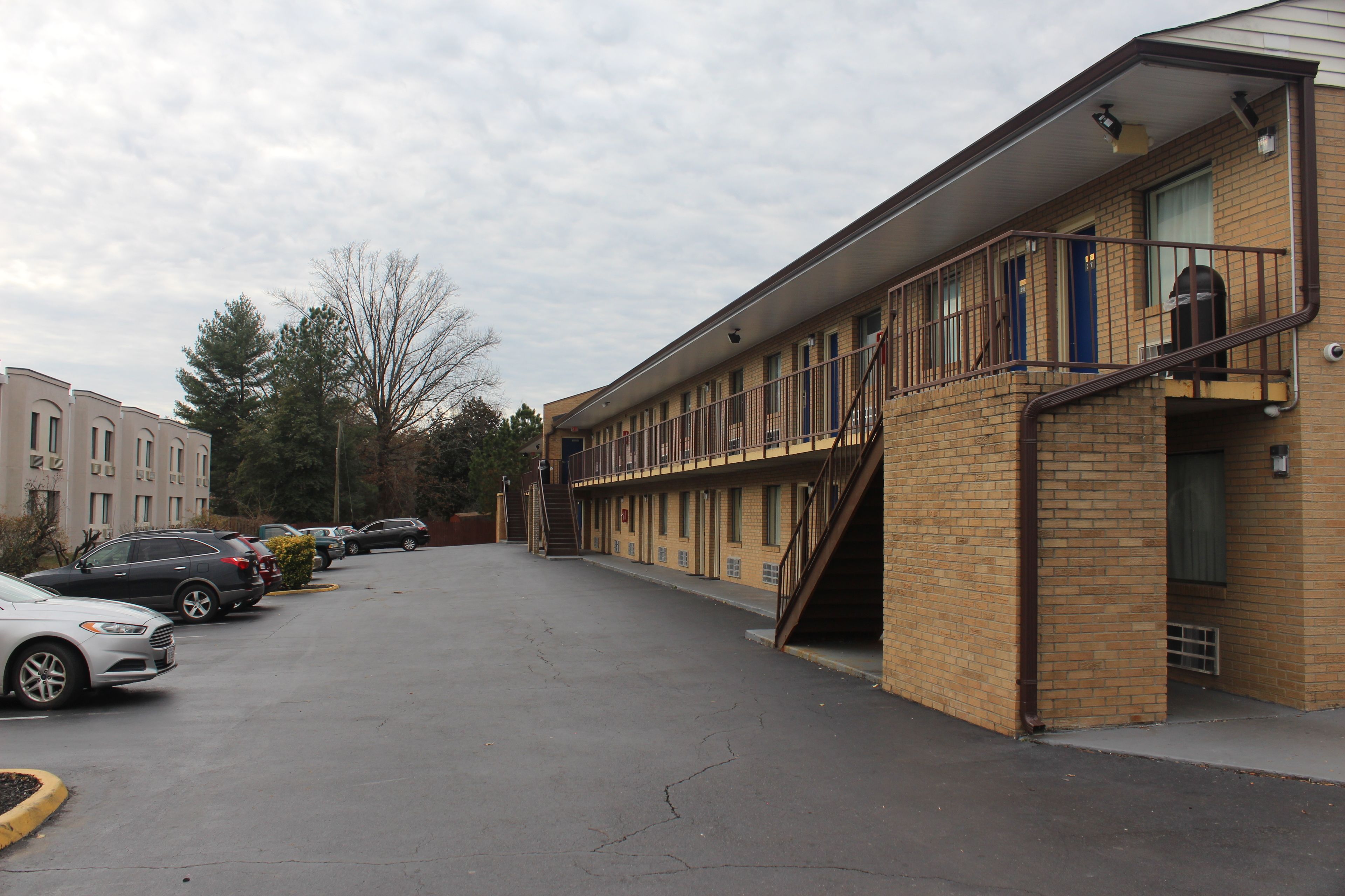 A motel with a brick exterior, a covered parking area, and a staircase leading to the entrance.