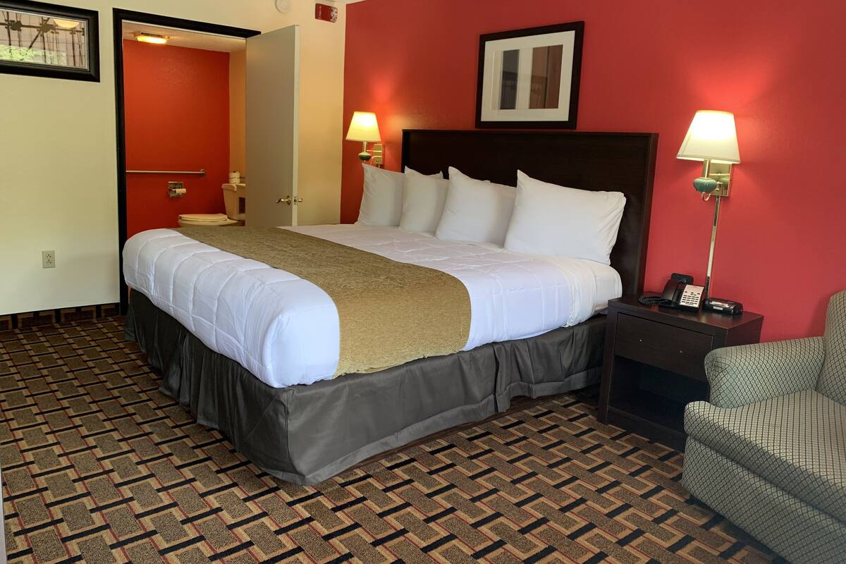 A hotel room with a large bed, two bedside lamps, a chair, and a red accent wall.