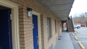 A building with a brick facade, numbered room doors, a covered walkway, and a parking lot. - Americas Best Value Inn Fredericksburg N (Fredericksburg)