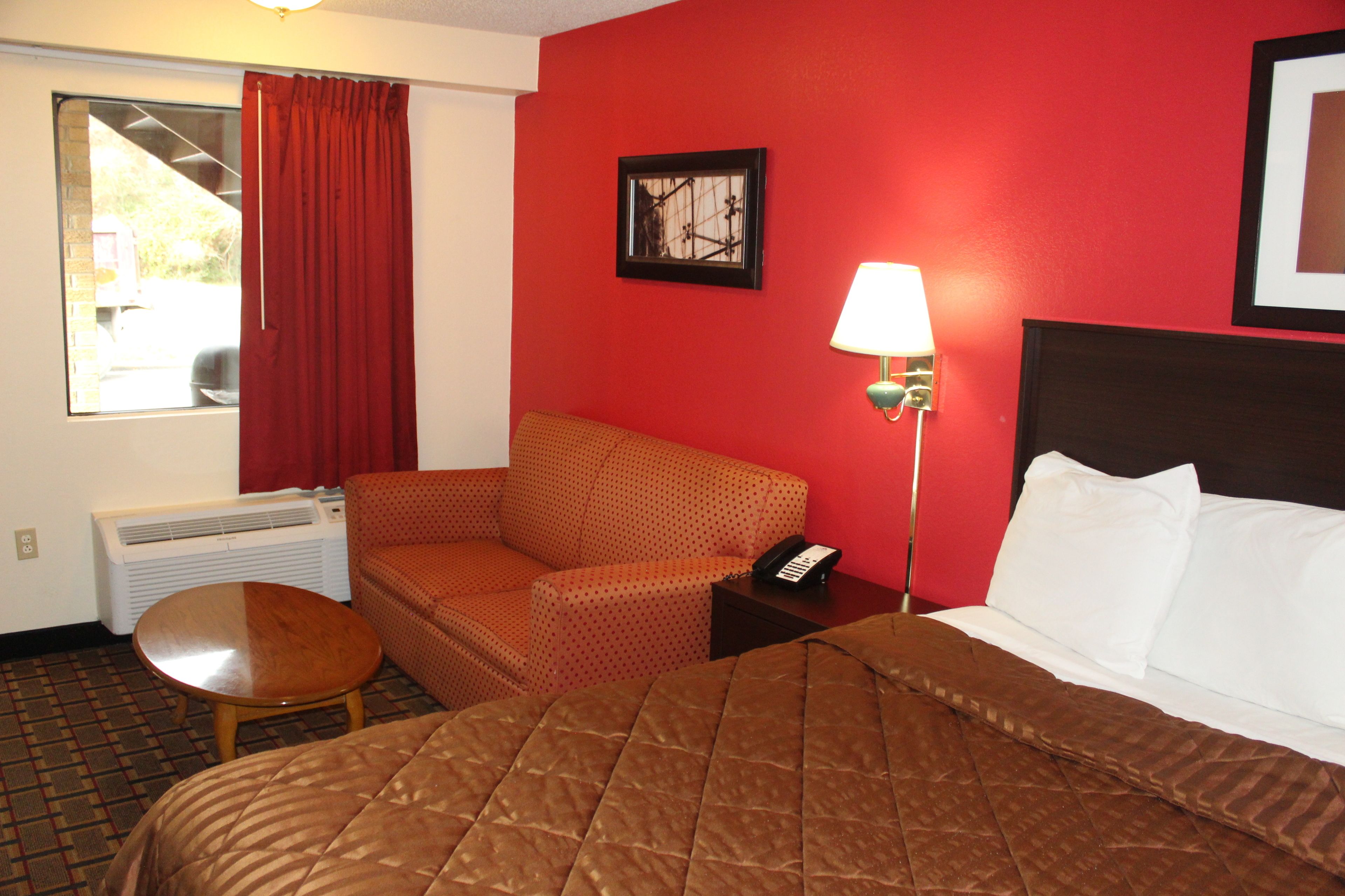 A hotel room with a bed, a chair, a small table, a lamp, and a picture on the wall.