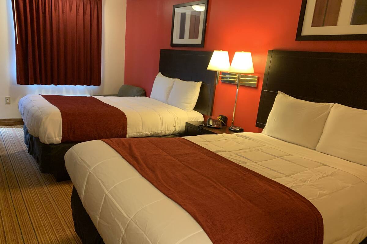 A hotel room with two beds, each with white and brown bedding, a nightstand with a lamp, and a framed picture on the wall.