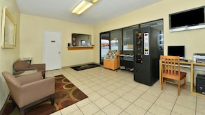A reception area with a reception desk, a vending machine, a wooden chair, and a door. - Americas Best Value Inn Fredericksburg N (Fredericksburg)