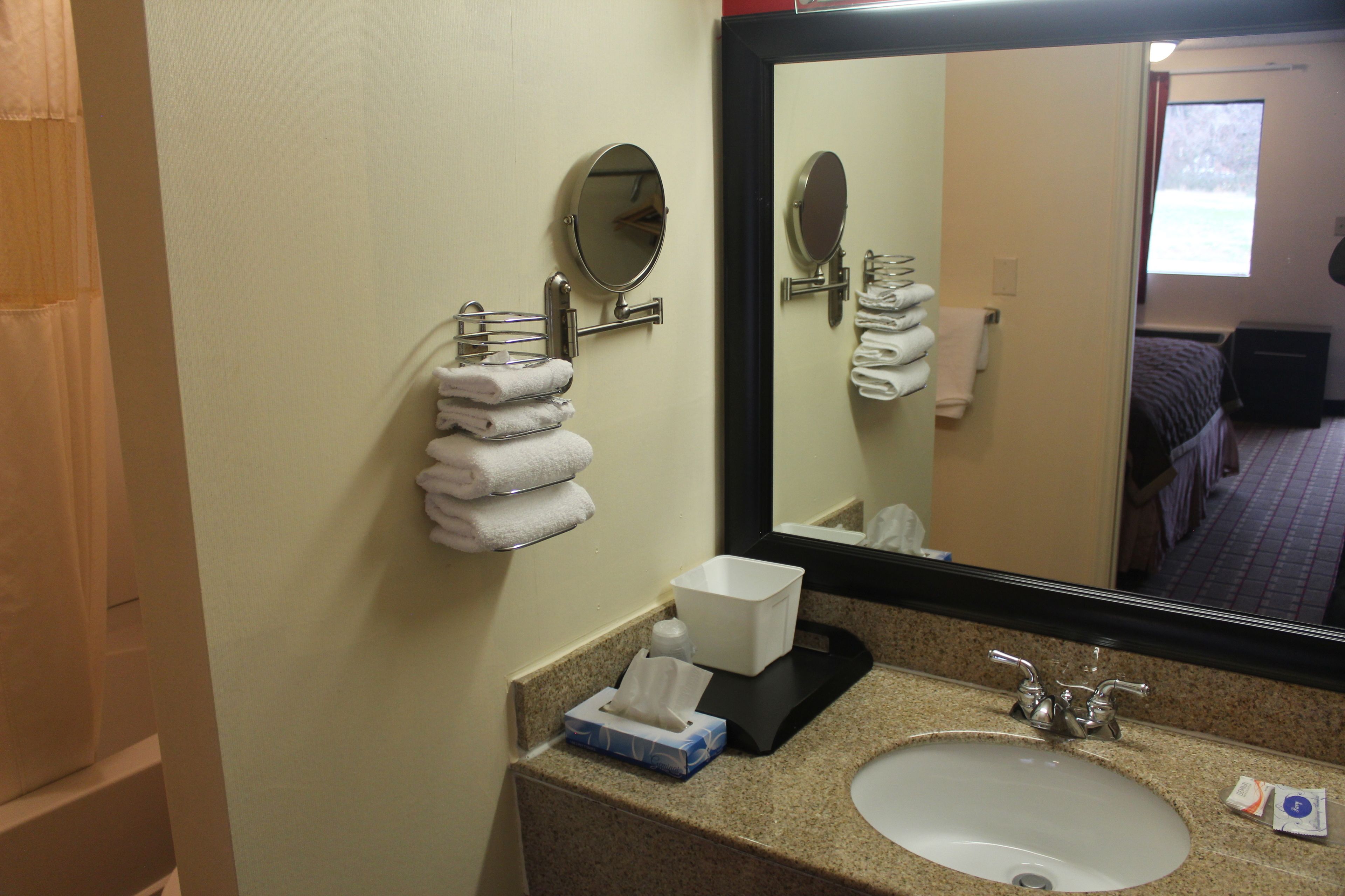A hotel bathroom with a sink, mirror, towel rack, and a window with a view of a building.