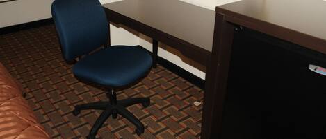 A hotel room with a bed, a desk, a chair, and a small refrigerator.