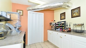 A kitchen with white cabinets, a countertop with coffee-making equipment, and a door. - Americas Best Value Inn Fredericksburg N (Fredericksburg)