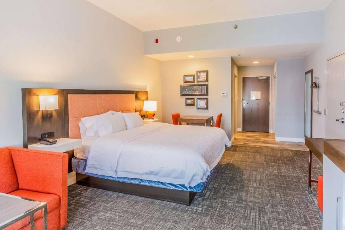 A hotel room with a bed, a desk, a chair, a table, and a door.