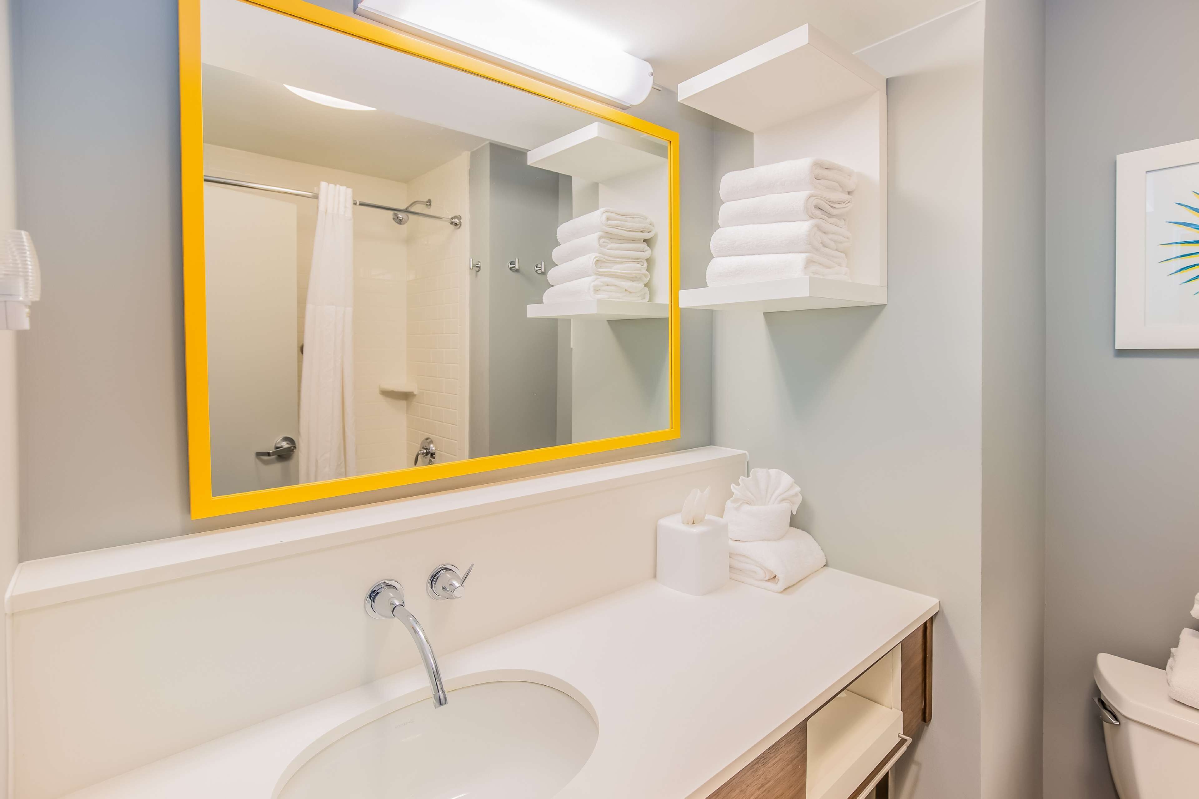 A modern bathroom with a large mirror, white sink, and neatly arranged towels.