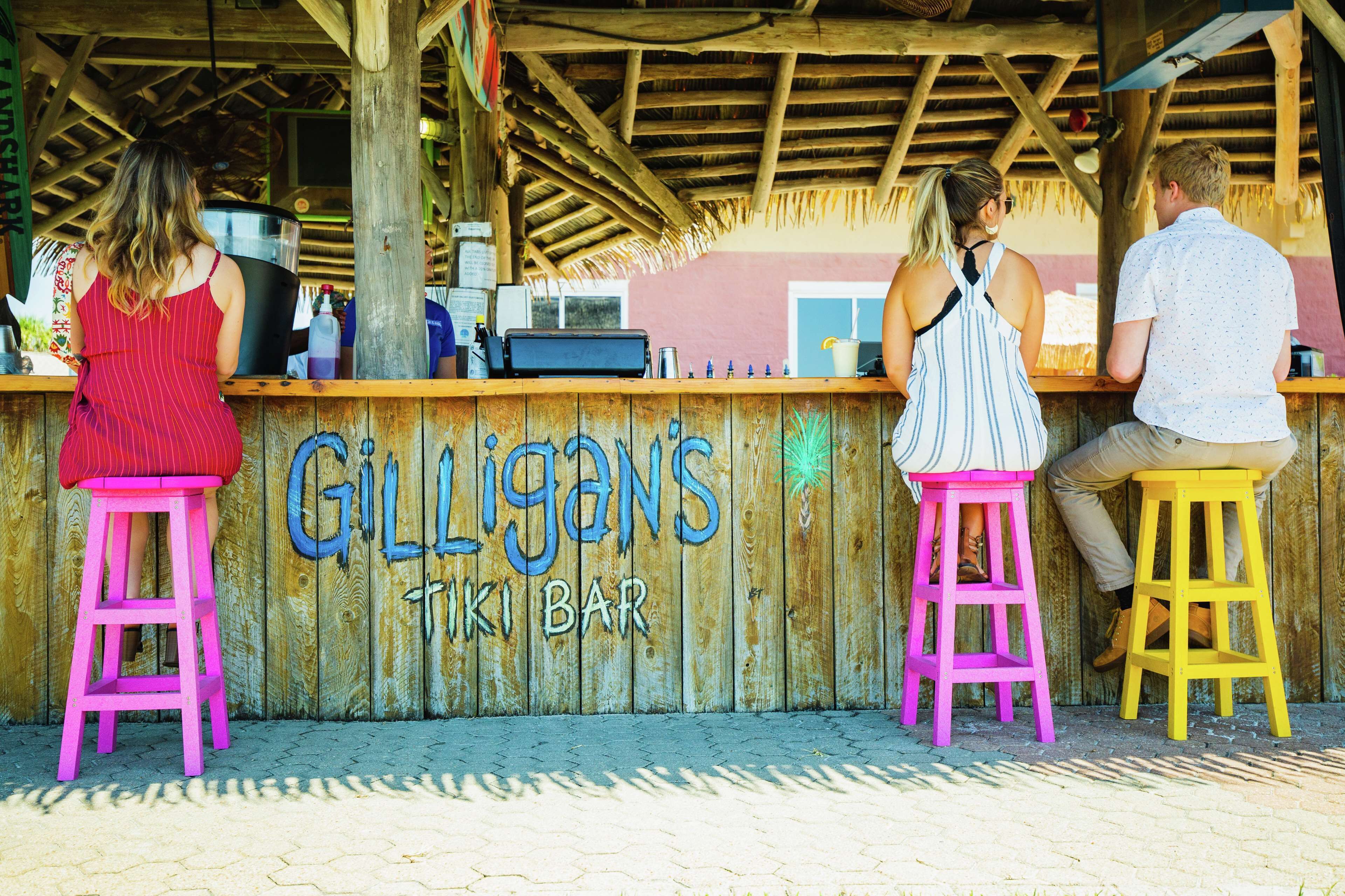 A wooden tiki bar with a sign reading "Gilligans Tiki Bar."