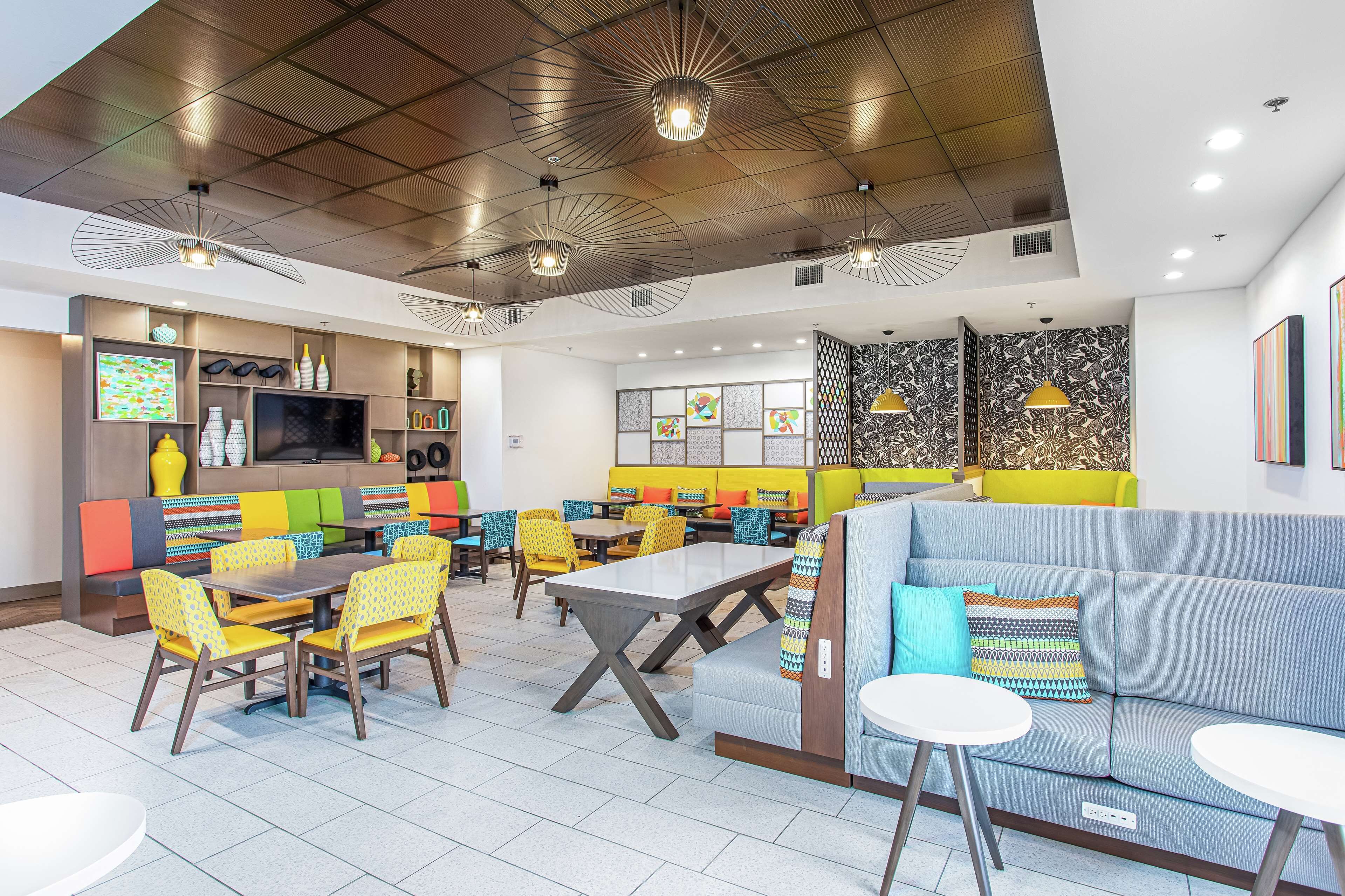 Un restaurante moderno con zona central de comedor, cabinas y barra con una pantalla de televisión grande.