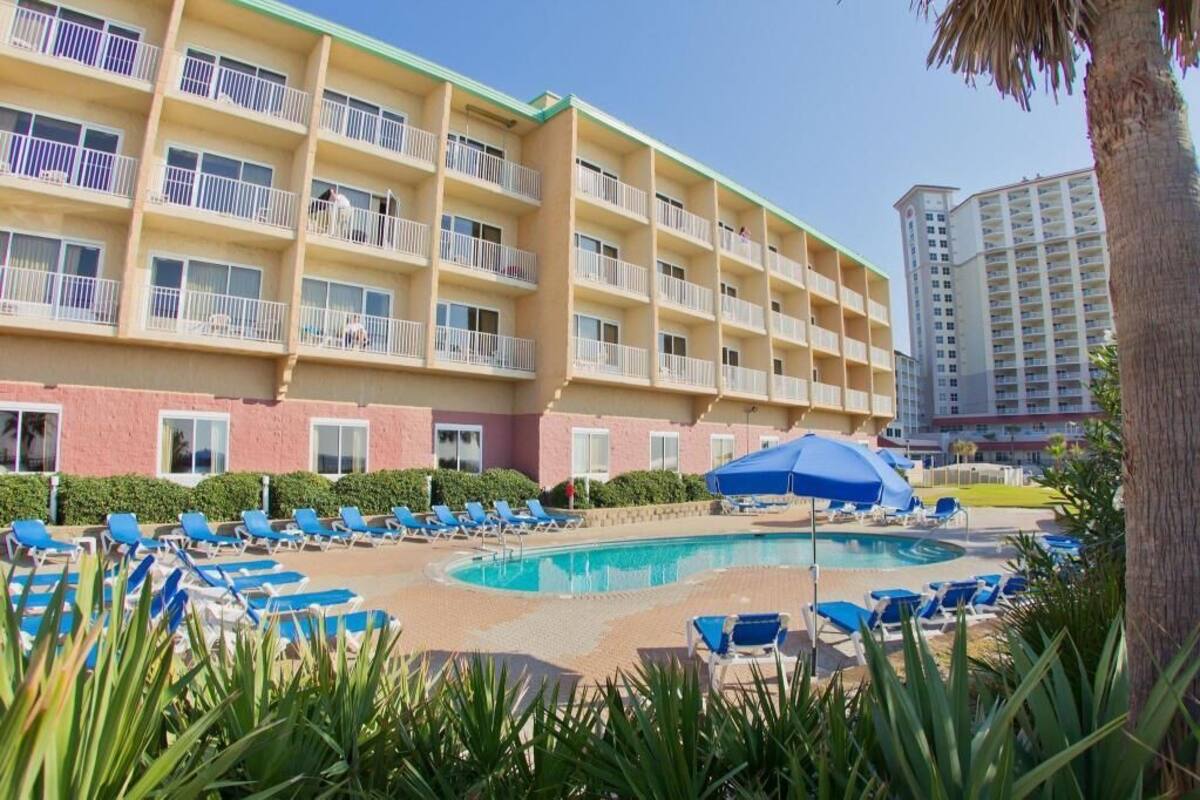 A hotel with a pool area, blue lounge chairs, and a large building with balconies.