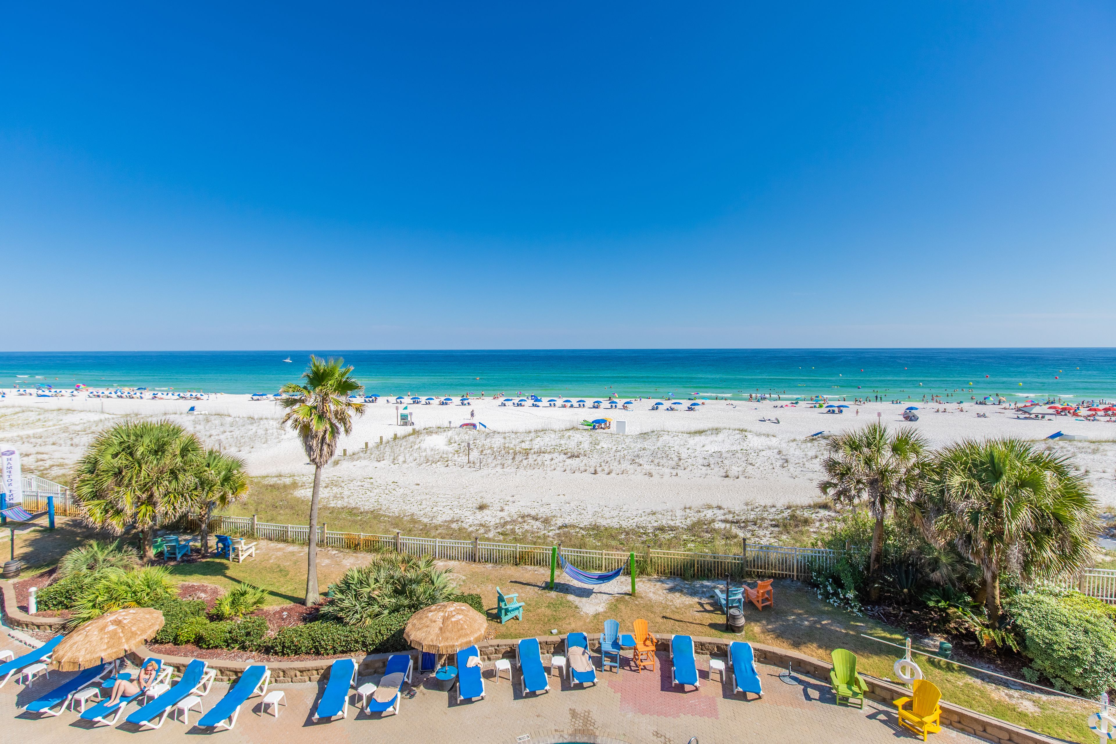 A beach resort with sun loungers, palm trees, and a view of the ocean.