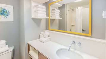 Un baño moderno con un lavamanos blanco, un espejo grande con marco amarillo y repisas con toallas blancas.