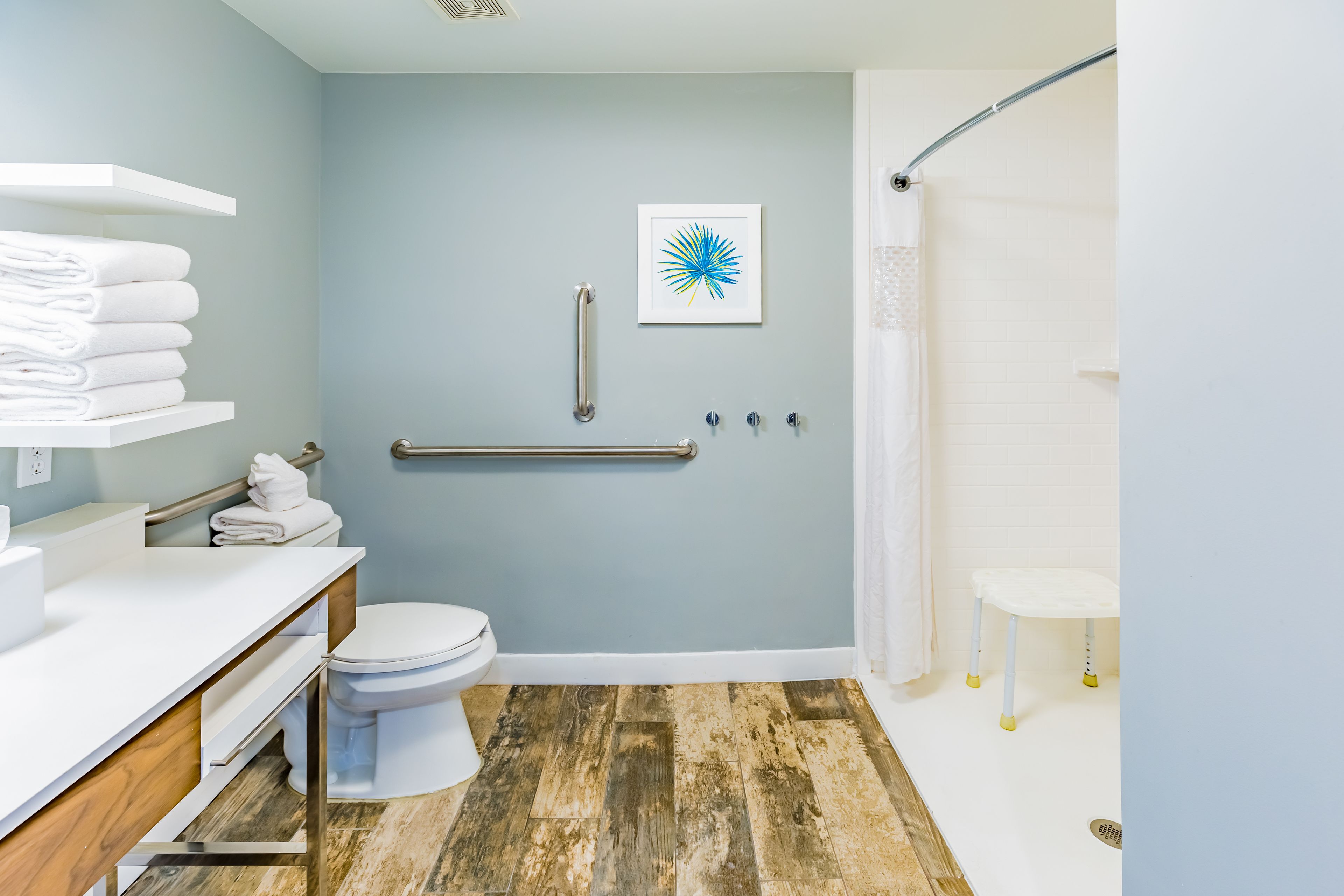 A bathroom with a toilet, a sink, a shower, and a handrail.