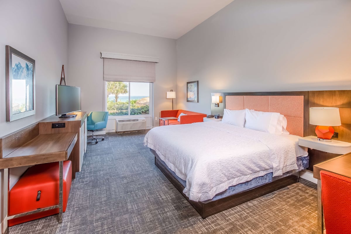 A hotel room with a large bed, a desk with a computer, a chair, and a window with a view of the outdoors.